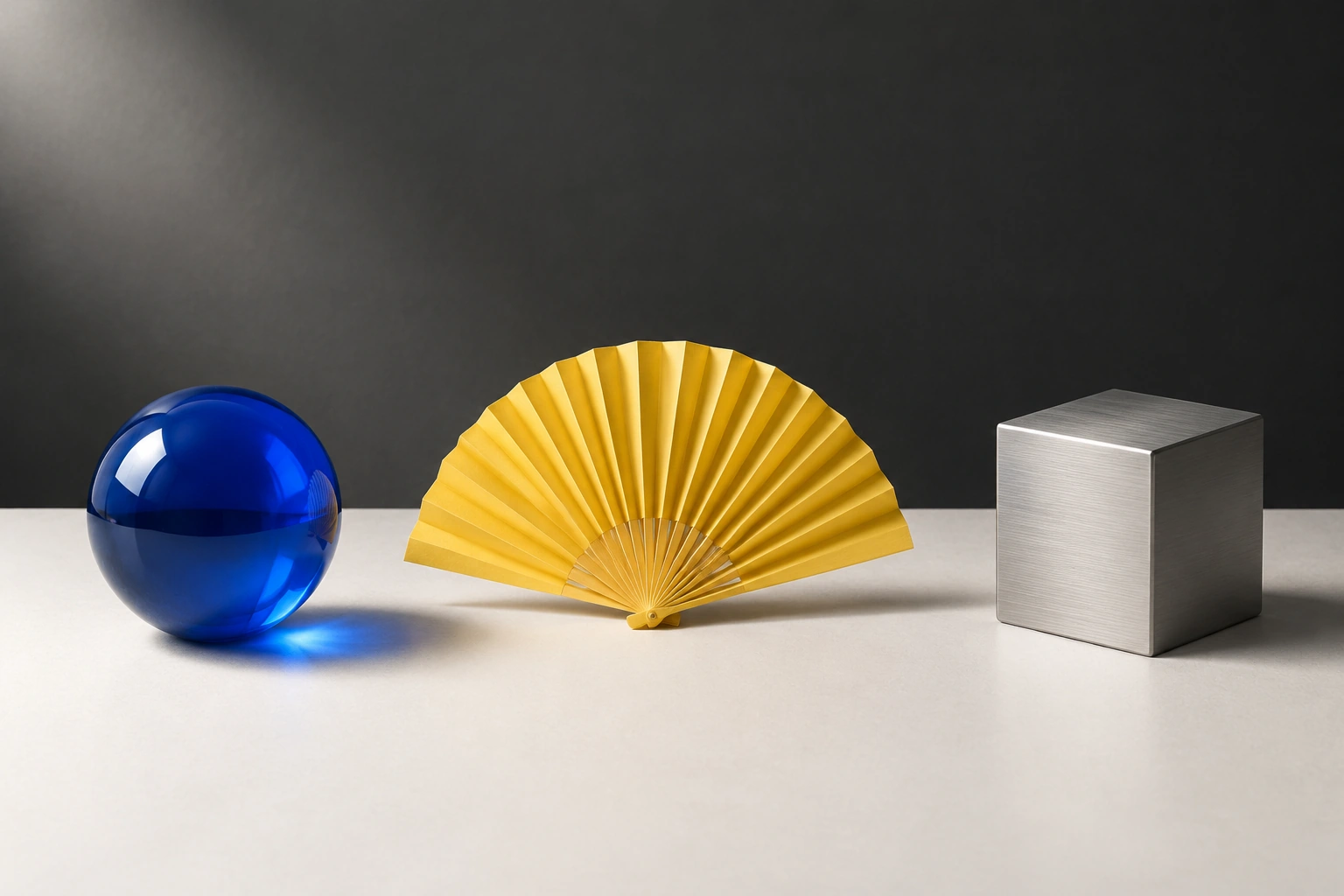 Blue glass sphere, yellow folded fan, and steel cube in the requested order
